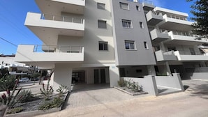 A multi-story building with balconies, a gated entrance, and a paved driveway. - Vasili's Mini Villa in Nafplio With Shaded Parking (Nafplio)