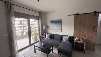 A modern living room with a sofa, coffee table, and a view of a balcony.