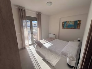 A hotel room with a bed, a window with curtains, a radiator, and a painting on the wall. - Vasili's Mini Villa in Nafplio With Shaded Parking (Nafplio)