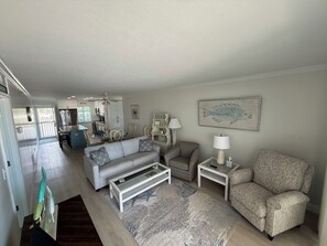 A living room with a sofa, armchairs, a coffee table, and a dining area with a table and chairs. - Just Listed - Enjoy sunset every night with direct beach and pool access. (Fort Myers Beach)