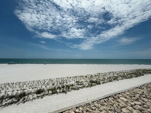 A beach with a clear sky, a sandy shore, and a rocky path. - Just Listed - Enjoy sunset every night with direct beach and pool access. (Fort Myers Beach)
