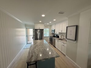 A modern kitchen with a marble countertop, stainless steel appliances, and white cabinetry. - Just Listed - Enjoy sunset every night with direct beach and pool access. (Fort Myers Beach)