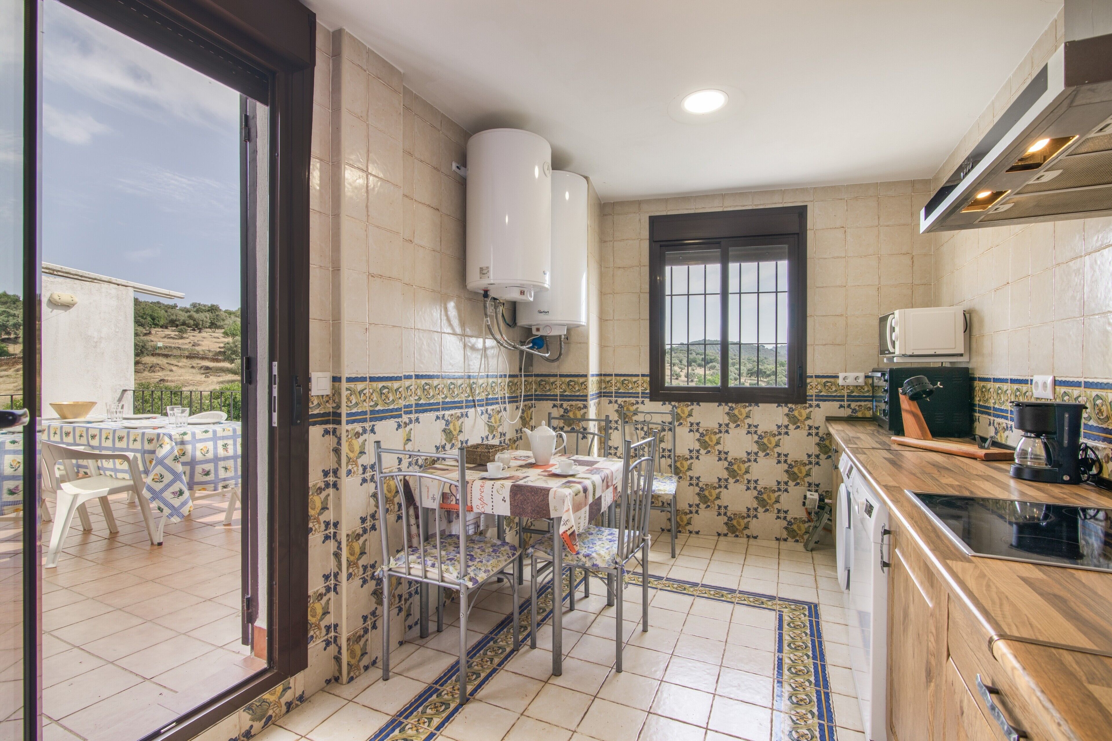Una cocina con paredes de azulejos, una mesa de comedor con sillas, una ventana y un calentador de agua.