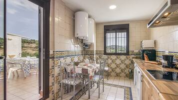 Una cocina con paredes de azulejos, una mesa de comedor con sillas, una ventana y un calentador de agua.