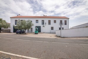 A two-story building with a red-tiled roof, a green door, and a parked car in front. - El Corralón de Severo – Rural House for Groups (Hinojales)