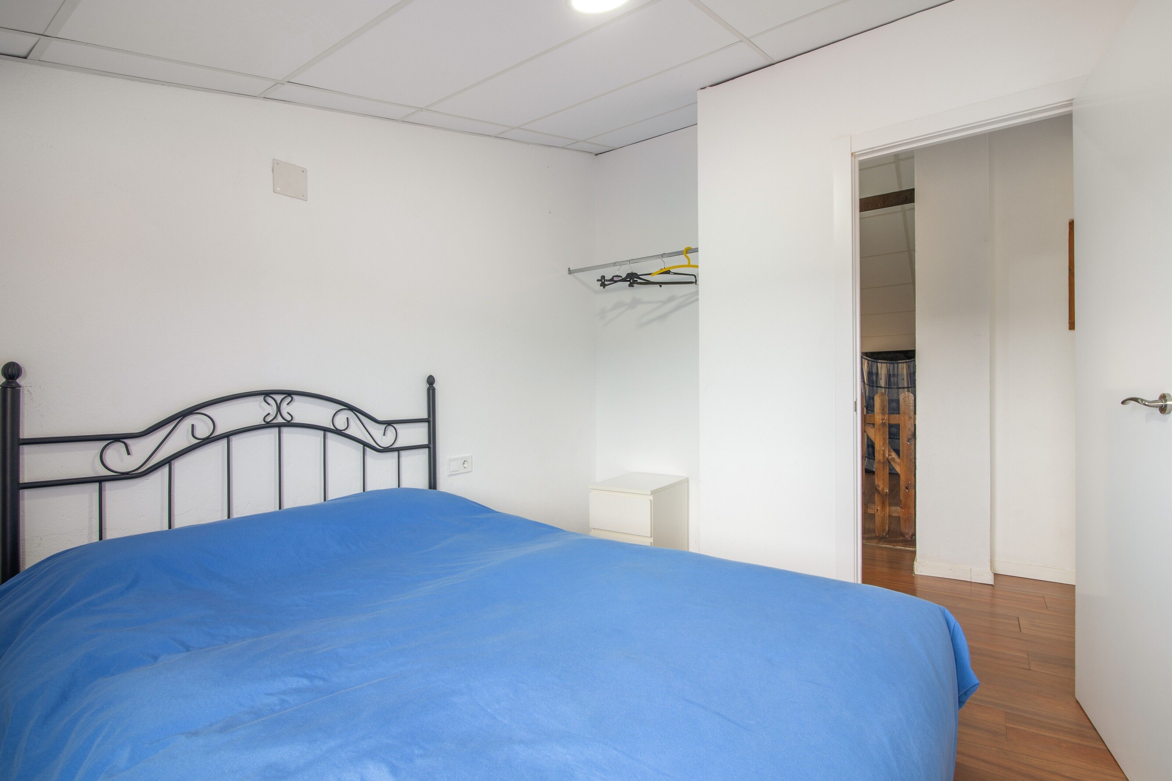 Un dormitorio con cama, mesita de noche, armario y puerta que da a otra habitación.