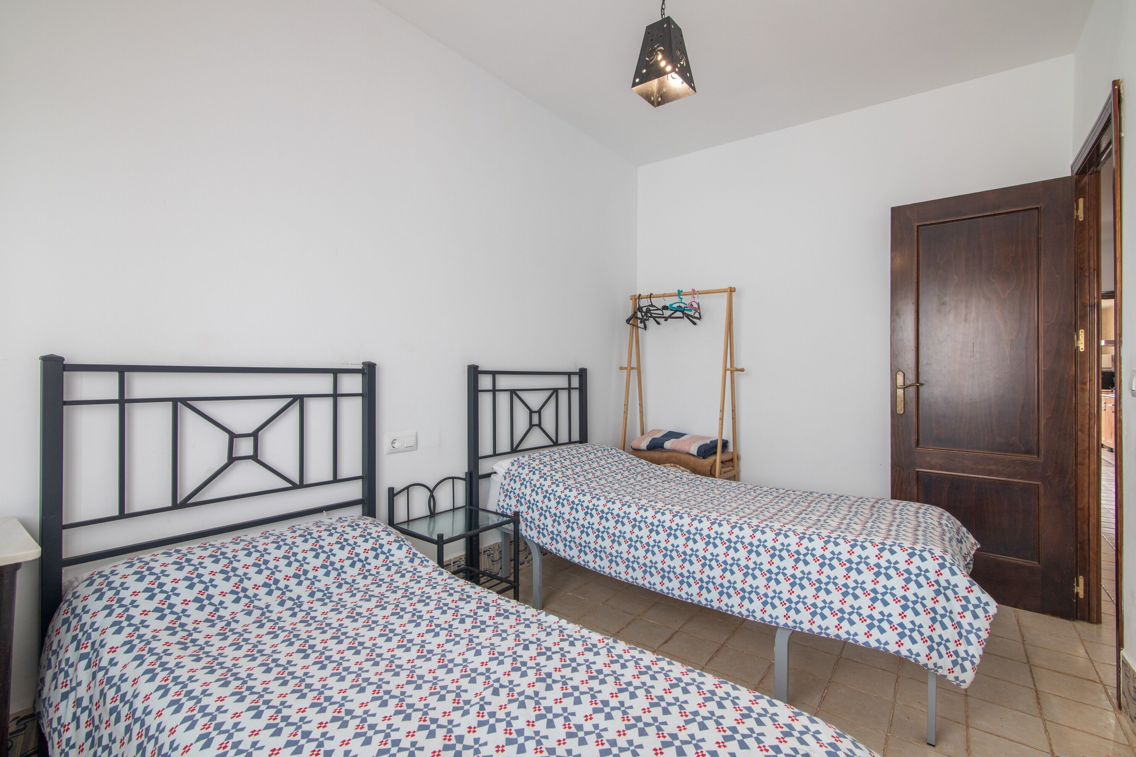 Una habitació amb dos llits, una porta de fusta i un llum penjant.