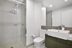 A modern bathroom with a glass shower enclosure, a toilet, a sink, and a mirror. - Elevated 1-bed Retreat Near Crown (Melbourne)