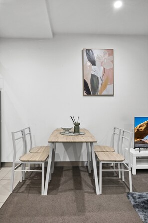 A dining area with a table and chairs, a painting on the wall, and a television on the right. - Elevated 1-bed Retreat Near Crown (Melbourne)