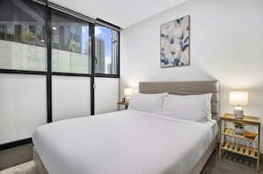 A hotel room with a large bed, two bedside lamps, a nightstand with a lamp, a wall-mounted painting, and a window with a city view. - Elevated 1-bed Retreat Near Crown (Melbourne)