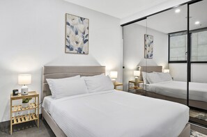 A hotel room with a large bed, two bedside tables with lamps, a small shelf with a plant, and a large mirror. - Elevated 1-bed Retreat Near Crown (Melbourne)