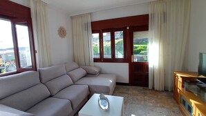 A living room with a sofa, a coffee table, a TV stand, and a window with curtains. - Apartment with sea view (Campelo)