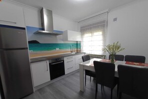 Een moderne keuken met witte kasten, een roestvrijstalen koelkast en een eethoek met een witte tafel en zwarte stoelen.