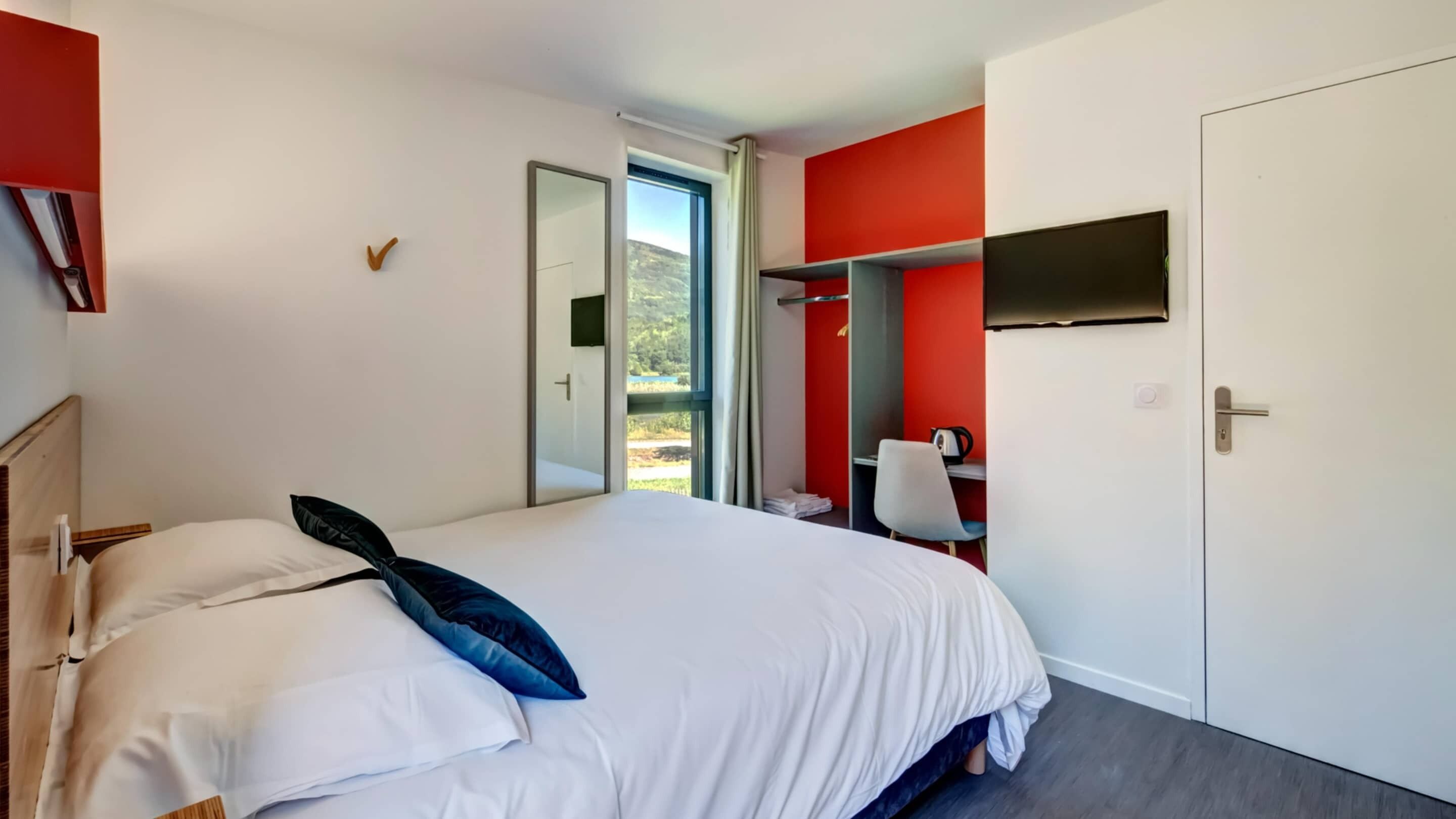 A hotel room with a bed, a desk, a chair, a TV, and a wardrobe.