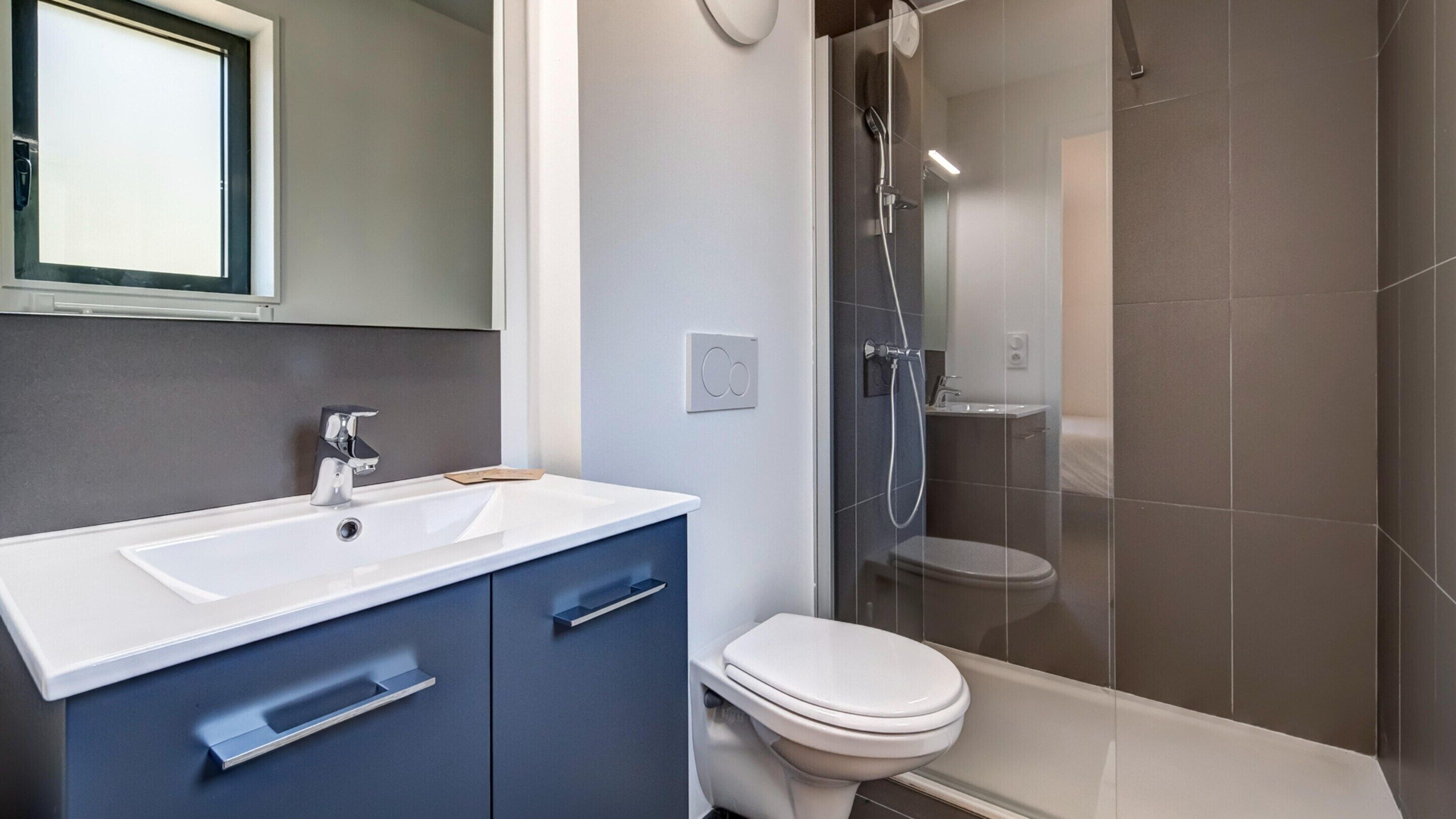 Ein modernes Badezimmer mit einem weißen Waschbecken, blauen Schränken, einer Toilette und einer Duschkabine aus Glas.