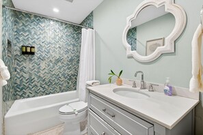 Une salle de bain avec un mur recouvert de carreaux disposés en motif chevron, une baignoire sur pieds, un meuble-lavabo avec un miroir et des toilettes.