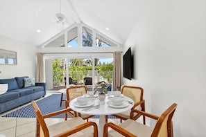 A modern living room with a dining area, a TV mounted on the wall, and a view of the outdoors.