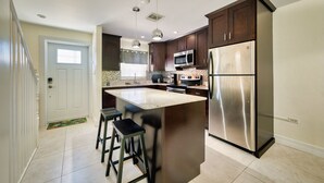 A modern kitchen with a central island, stainless steel appliances, and a staircase leading to another level. - 2BR/2BA Peaceful Retreat, Patio, Walk to Beach (West Bay)