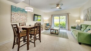 A dining area with a table and chairs, a sofa, a ceiling fan, and a view through a glass door. - 2BR/2BA Peaceful Retreat, Patio, Walk to Beach (West Bay)