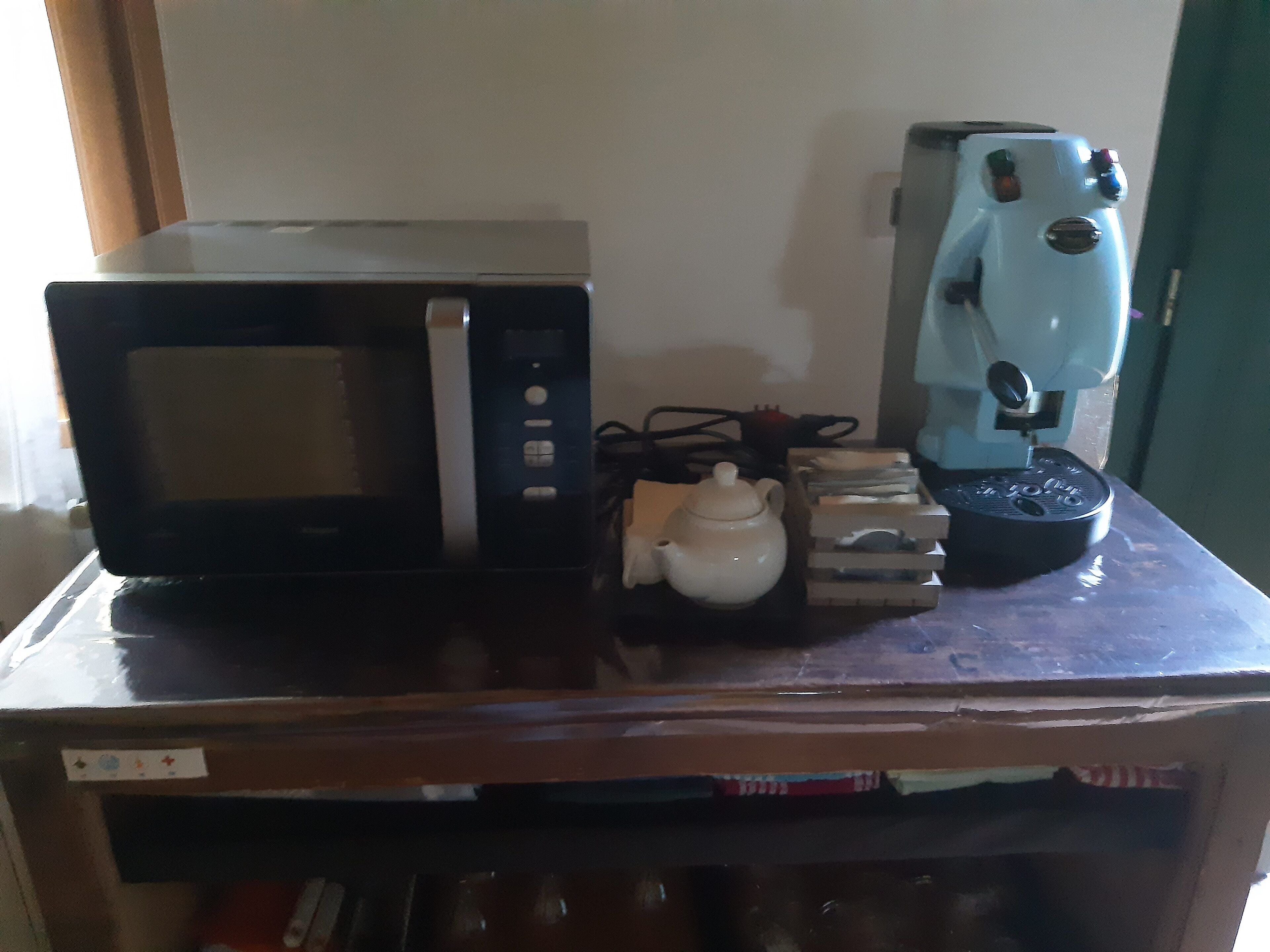 Un forno a microonde, una macchina da caffè, un bollitore e una pila di libri su un tavolo di legno.