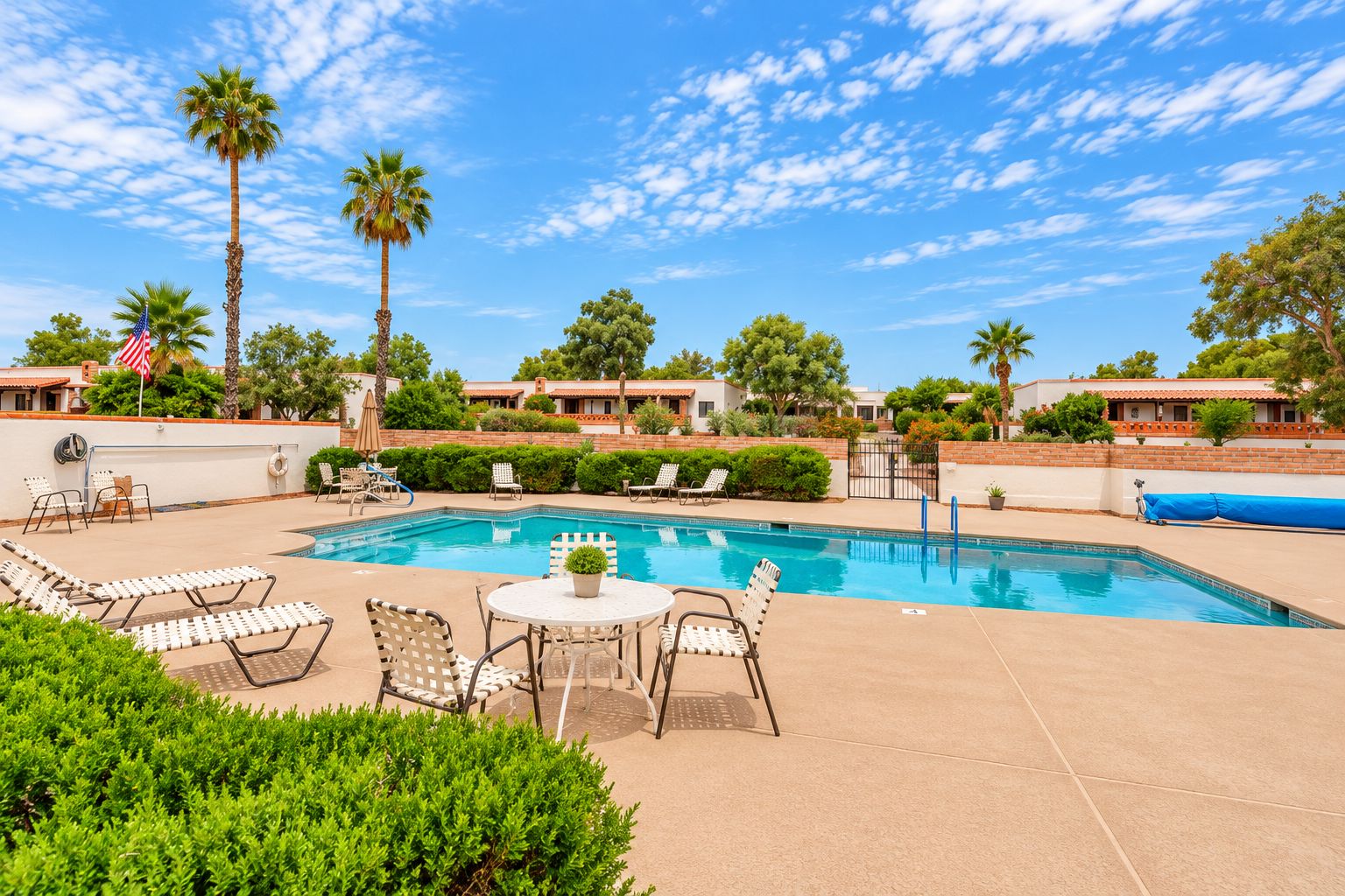 A swimming pool with lounge chairs and a table, surrounded by greenery and palm trees.