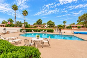 Una piscina con sillas de descanso y una mesa, rodeada de follaje y palmeras.