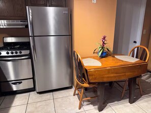 Eine Küche mit einem Edelstahl-Kühlschrank, Herd und Backofen, einem Holzespeisesatz mit Stühlen und einem Blumentopf auf dem Tisch.