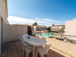 Un balcón con mesa y sillas, una piscina y edificios al fondo.