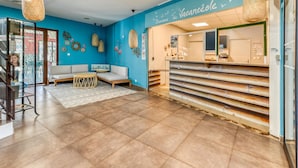 A reception area with a blue wall, a reception desk, a sofa, and hanging wicker lamps. - Pool View Apartment for Six (Le Grau-Du-Roi)