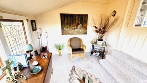 Una habitación acogedora con una mesa de madera, una silla de mimbre, un cuadro en la pared y una mesita con un florero.