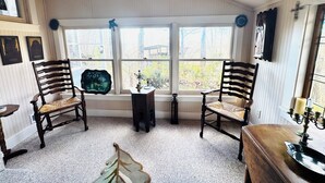 Una habitación con dos sillas de madera, una mesita y un ventanal con vistas a árboles y un edificio.