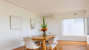 A dining area with a wooden table, white chairs, and a vase with flowers. - Metawise Stylish 2-bedroom Home With Easy CBD Ac (Point Clare)