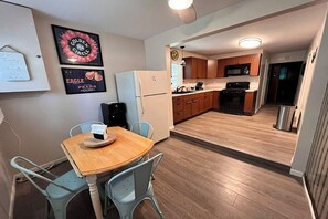 A compact kitchen with a refrigerator, microwave, and stove. There is a dining table with chairs.