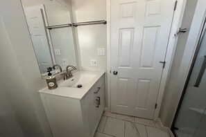 Un baño con lavamanos, espejo y puerta blancos.