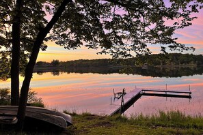 A serene lakeside view with a dock extending into the water, surrounded by trees and a clear sky.