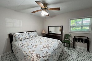 Un dormitorio con cama, ventilador de techo, espejo, silla y radiador.