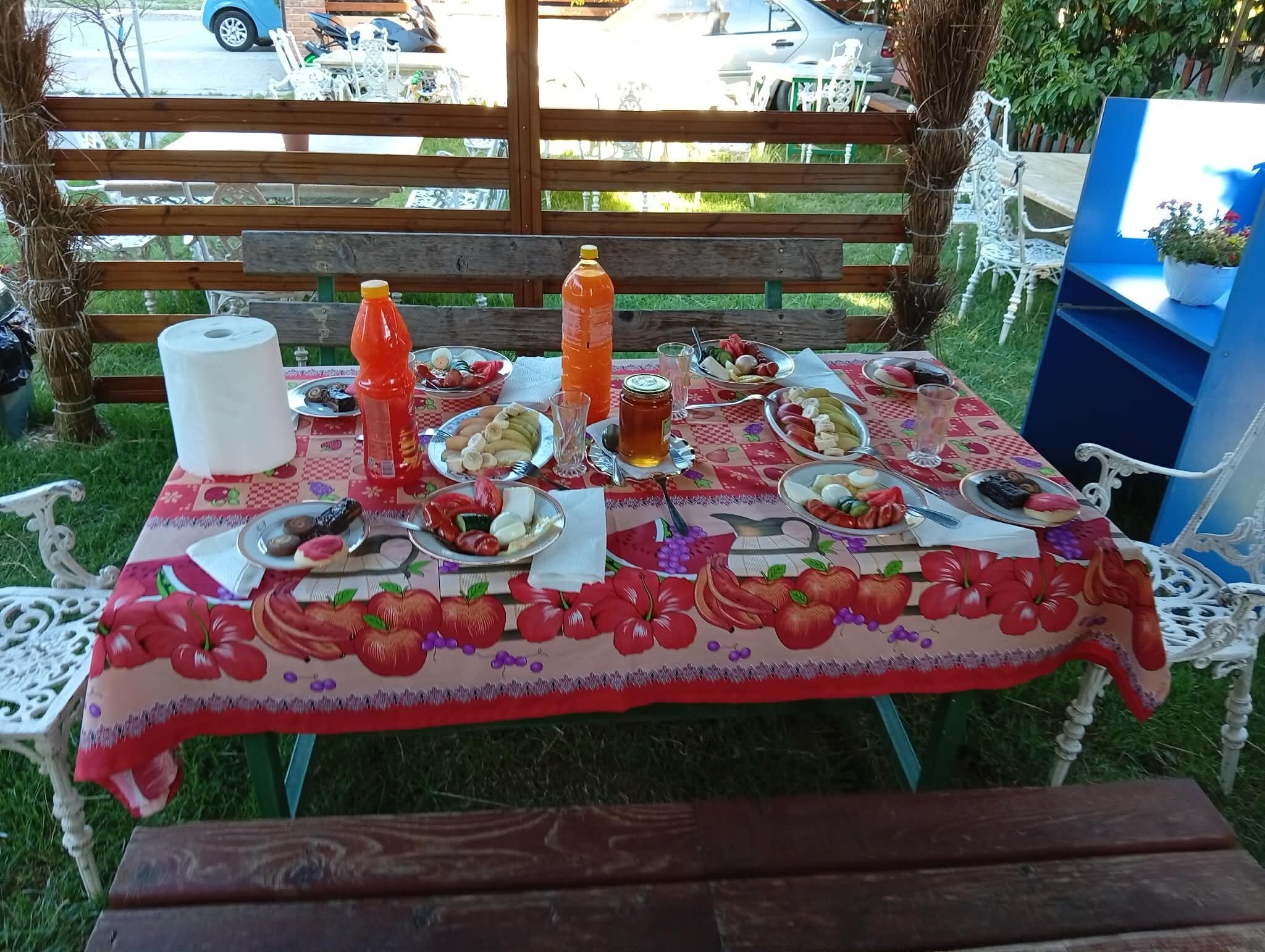 An outdoor dining table with a fruit-themed tablecloth, surrounded by white chairs.