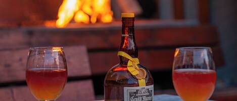 A bottle of Grand Marnier and two glasses on a table with a fire in the background.