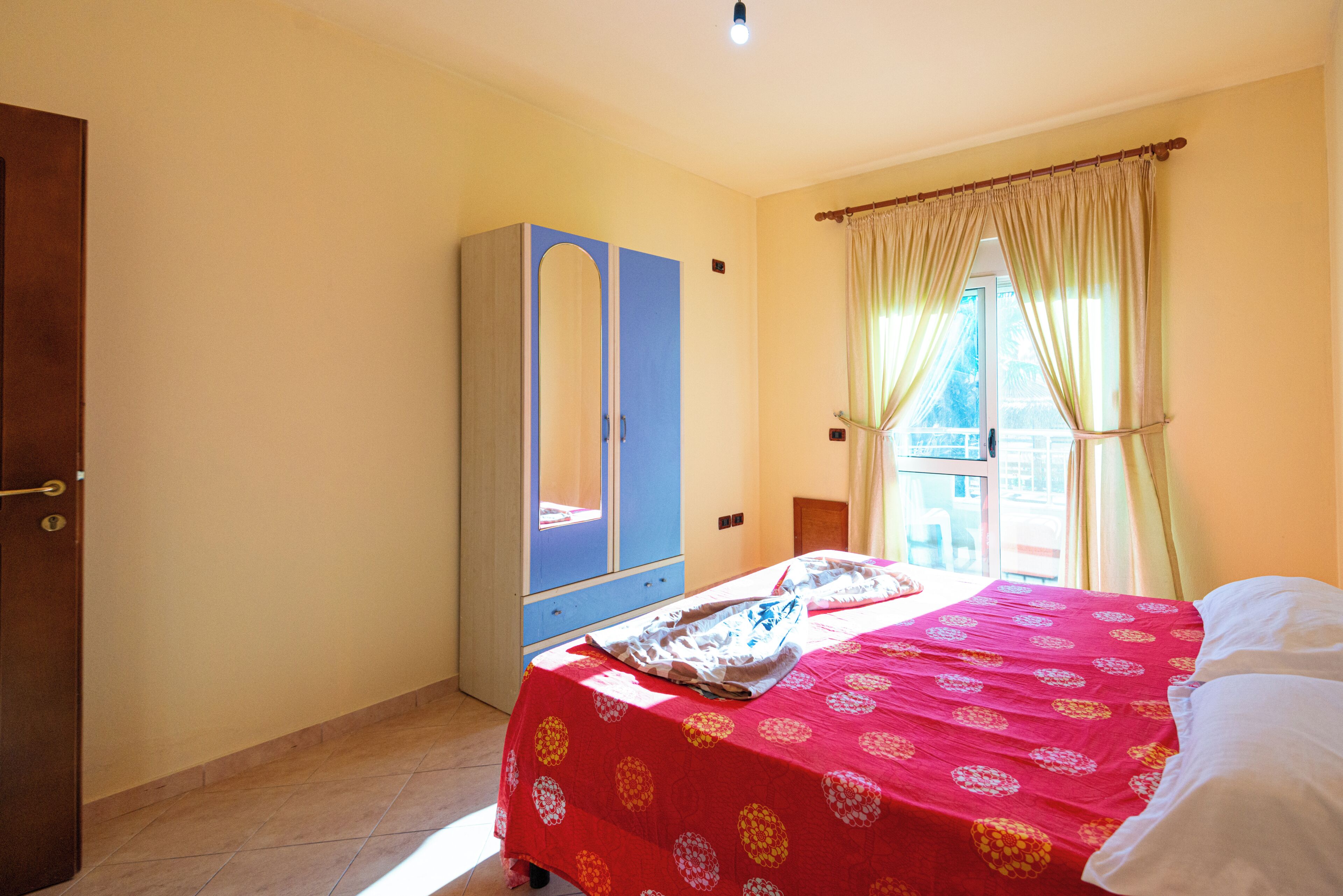 Un dormitorio con cama, armario y ventana con cortinas.