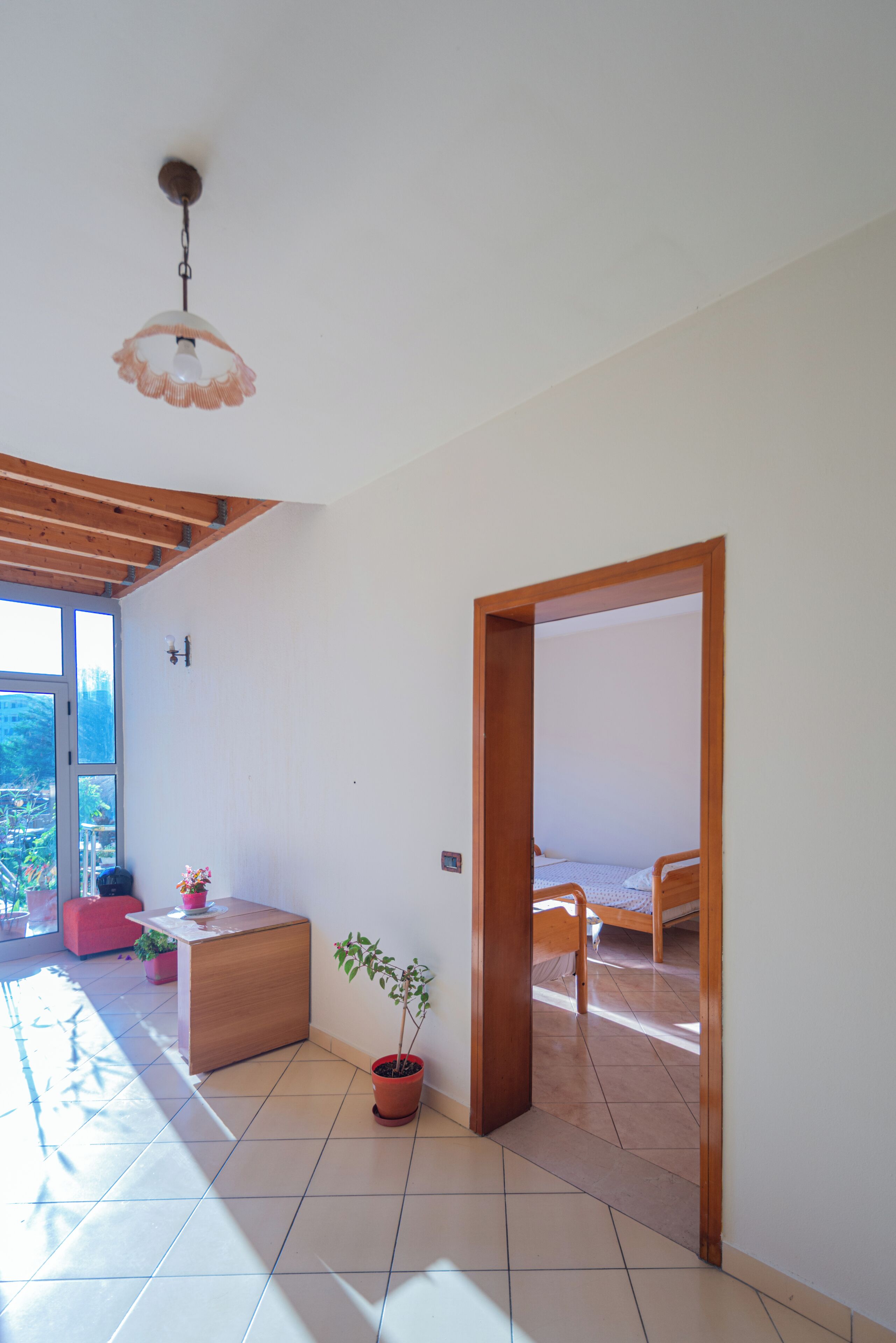 Una habitación con una cama, una planta en maceta, una mesita y vistas al exterior.
