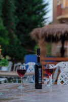 A table with a bottle and two glasses of red wine, set outdoors with a thatched roof and greenery in the background.