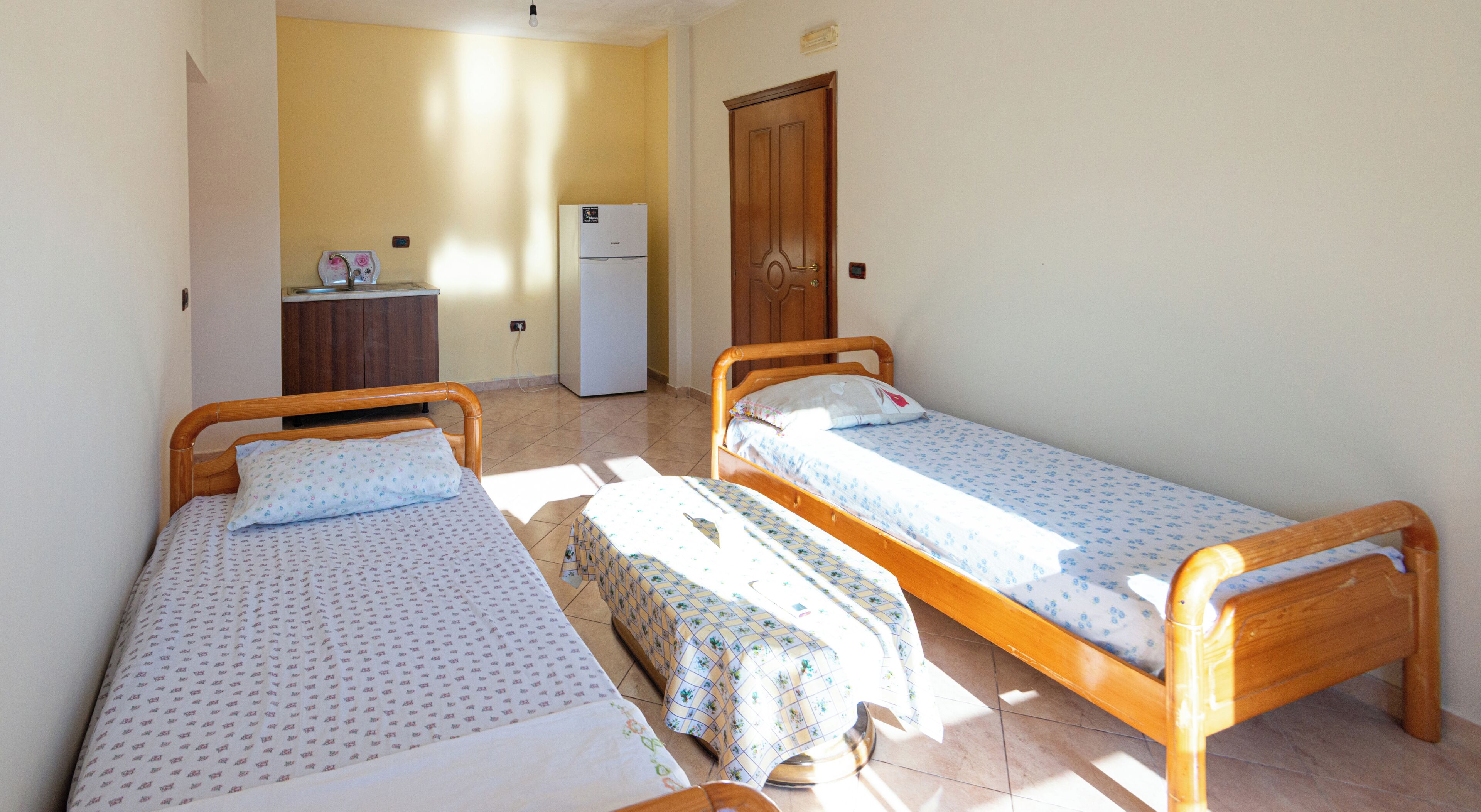 A room with two single beds, a small kitchenette, and a wooden door.