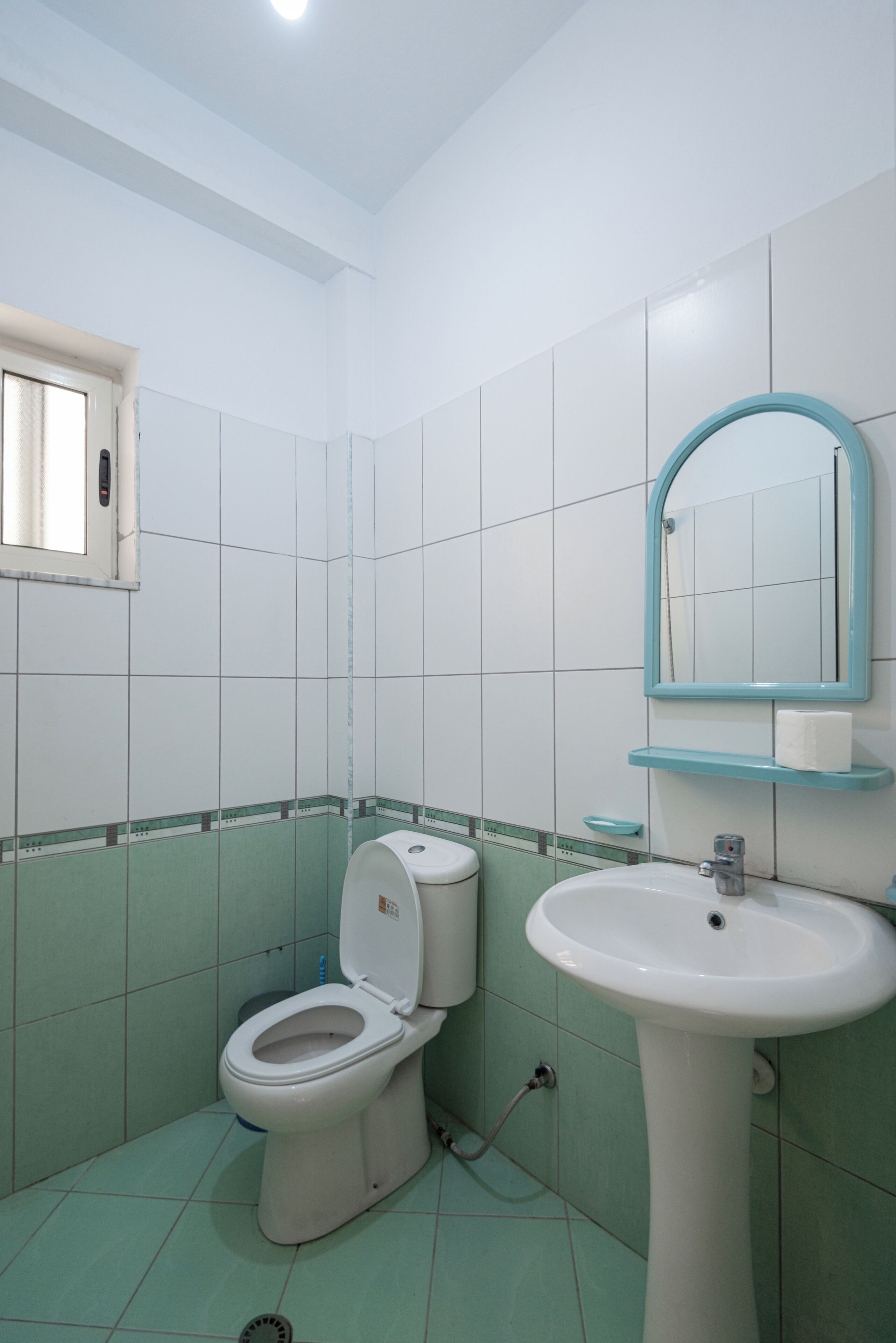 A bathroom with a toilet, sink, mirror, and tiled walls.