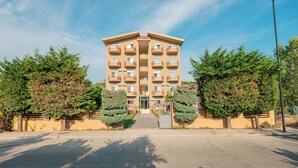 A multi-story building with balconies, a central entrance, and surrounding trees. - Serxhio Apartments Golem (Golem)
