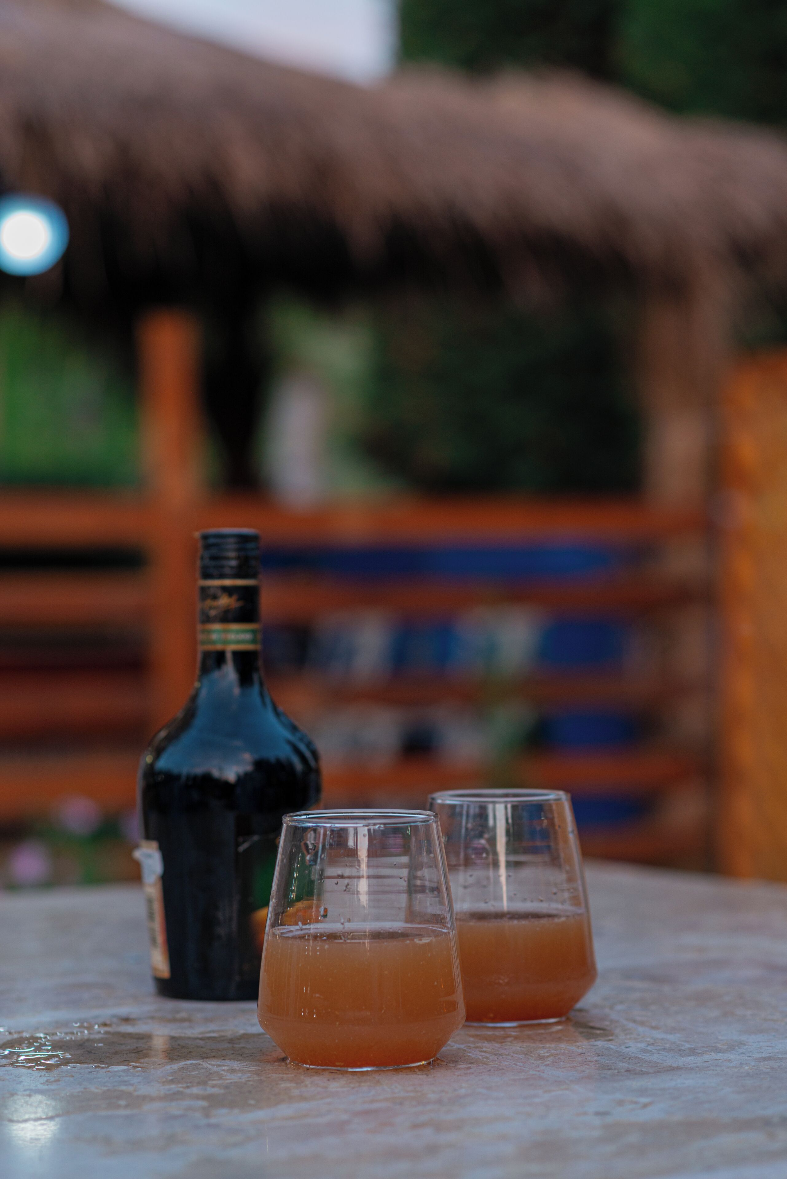 Een fles en twee glaasjes op een tafel, met een onscherpe achtergrond.