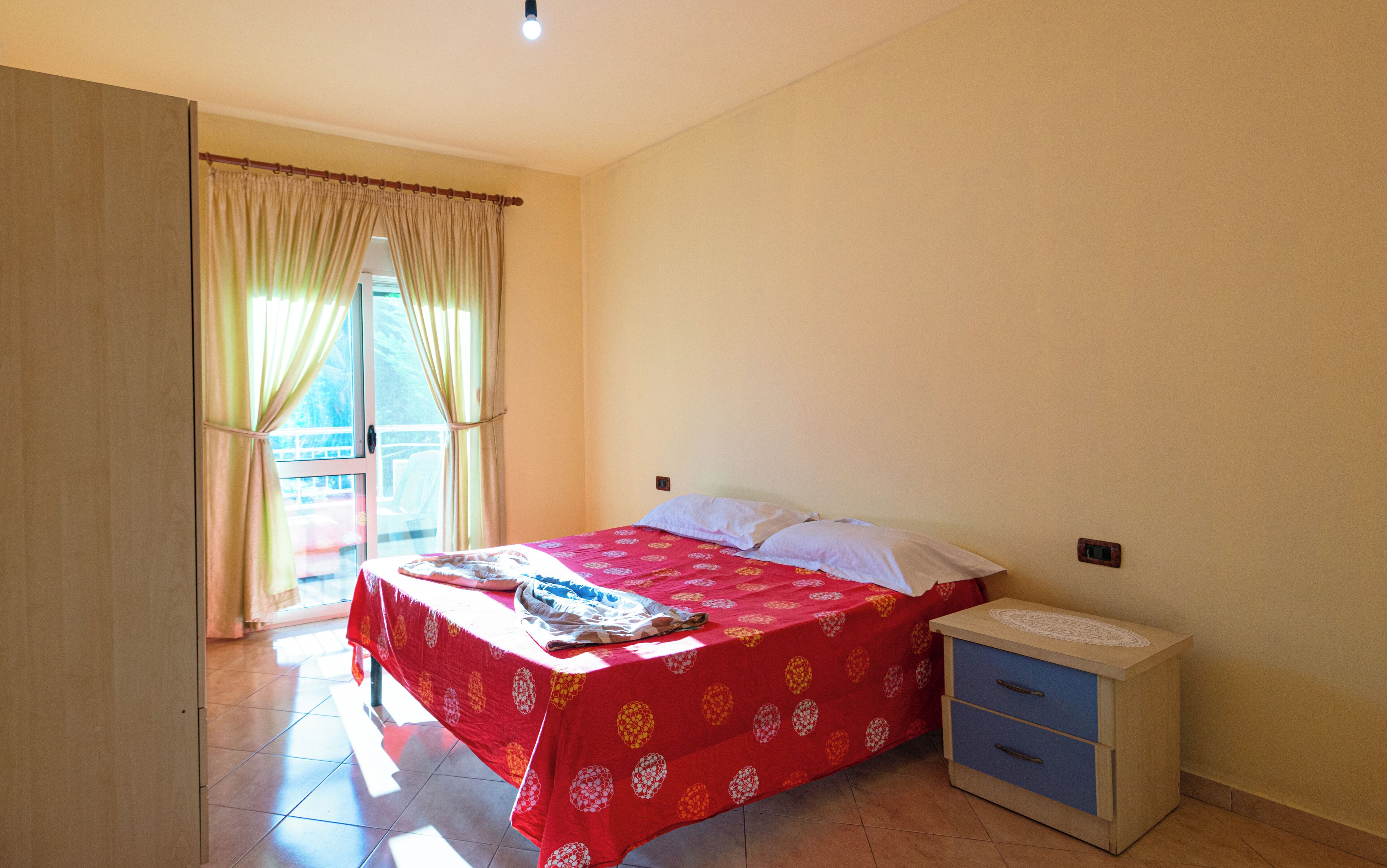 A bedroom with a bed, a bedside table, and a window with curtains.