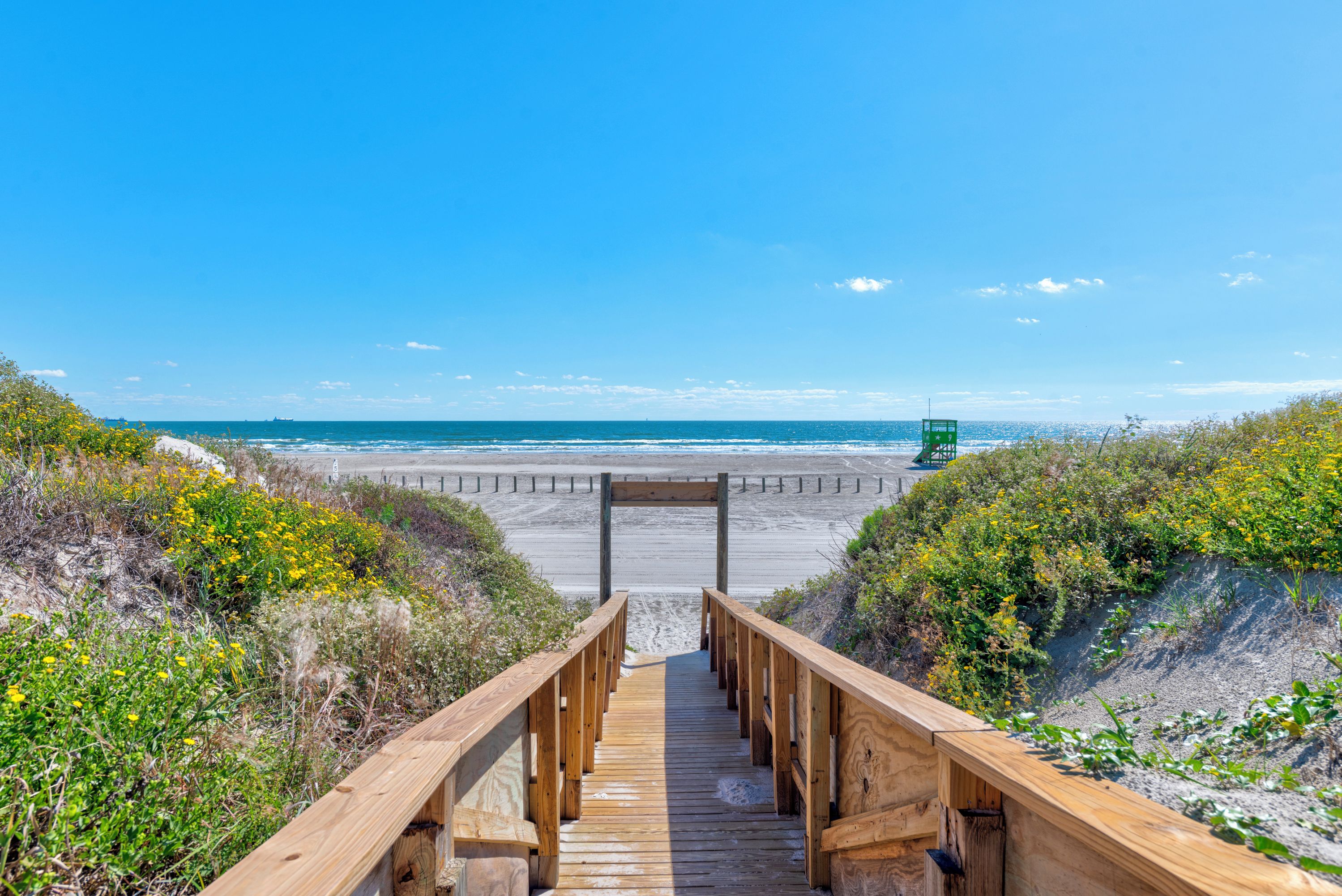 A wooden boardwalk leading to a beach with a lifeguard tower in the distance.