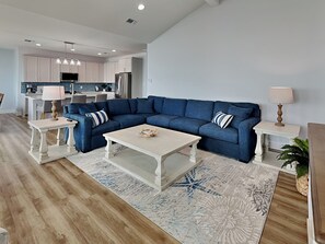 A modern living room with a sectional sofa, a coffee table, and a kitchen in the background. - Copano On The Rocks (Rockport)