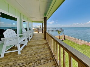 A wooden deck with white chairs, a view of the ocean, and a pier. - Copano On The Rocks (Rockport)