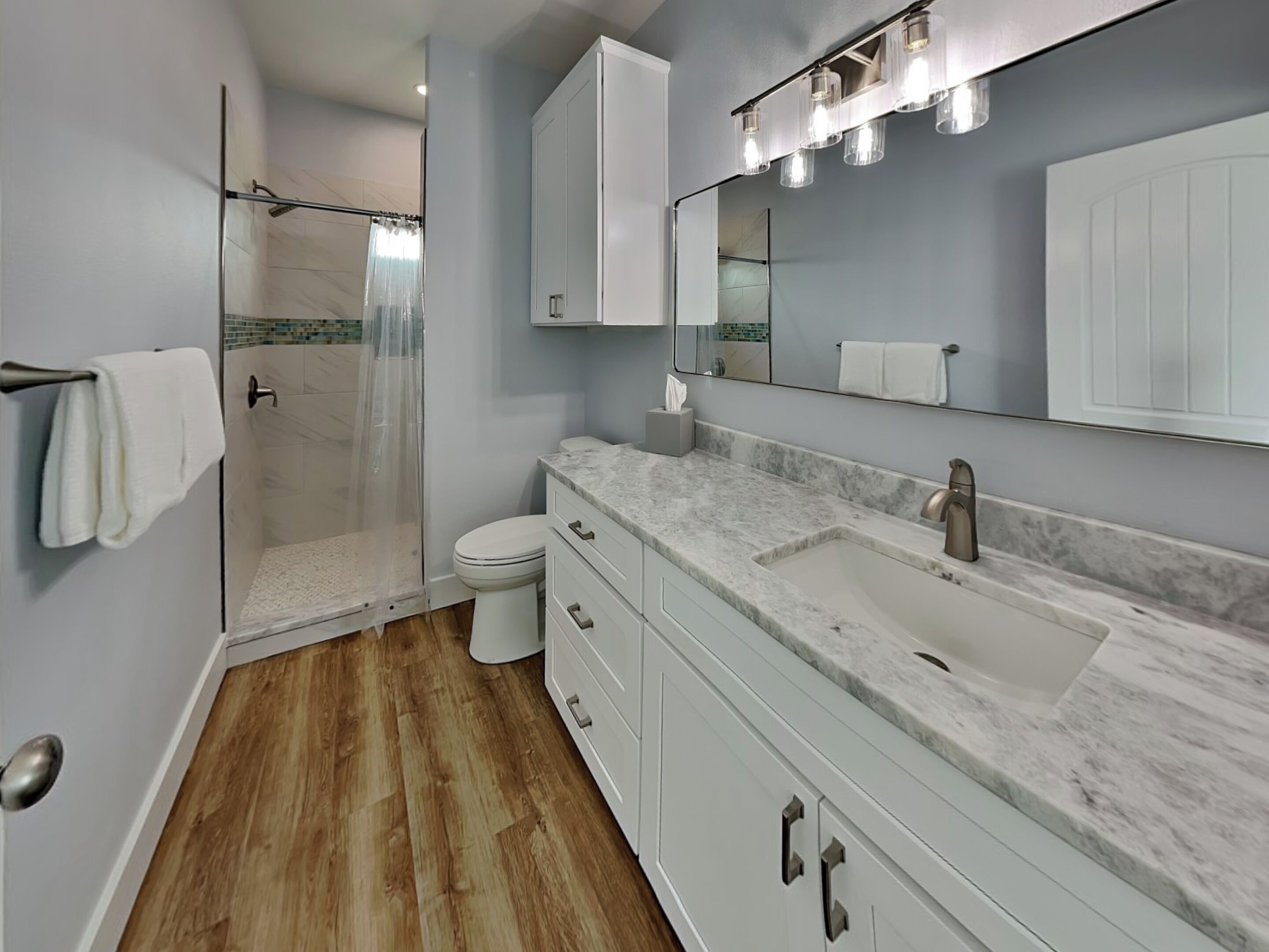 A modern bathroom with a shower, toilet, vanity, and a large mirror.
